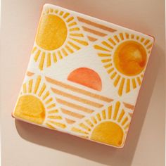 an orange and white square plate with sun designs on the front, sitting on a pink surface