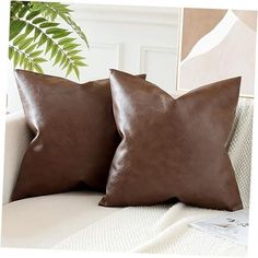 two brown leather pillows sitting on top of a white couch next to a green plant