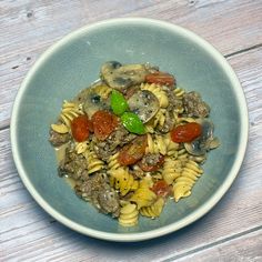 a bowl filled with pasta and mushrooms on top of a wooden table