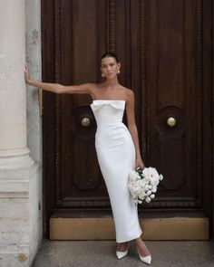 a woman standing in front of a door wearing a white dress and holding her arm out