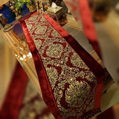 a red and gold table runner on display in front of a mirror with other items around it