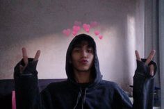 a man in a black hoodie holding two fingers up with hearts on the wall behind him