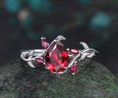 a close up view of a ring with red stones and leaves on the band, sitting on top of a rock