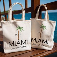 two bags with palm trees on them sitting on a wooden bench near the ocean and water