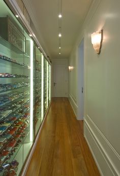 a long hallway with glass shelves filled with various types of shoes on the wall and wood flooring