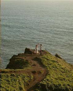 two people standing on top of a hill near the ocean