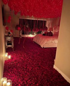 candles are lit in front of a bed with red carpet and balloons hanging from the ceiling