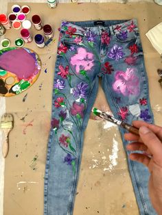 someone is painting flowers on their jeans with watercolors and paintbrushes next to them