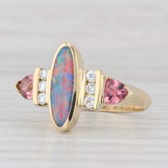 Gemstone Information: - Natural Opal - Size - 4 x 12.5 mm Cut - Oval Cabochon Color - Multicolor Please note the opal is cracked. This ring is being sold as is. - Natural Diamonds - Total Carats - 0.14ctw Cut - Round Brilliant Color - G - H Clarity - VS2 - Natural Tourmalines - Total Carats - 0.50ctw Cut - Trillion Brilliant Color - Pink Metal: 18k Yellow Gold Weight: 4.6 Grams  Stamps: 18k Face Height: 13.8 mm  Rise Above Finger: 4.4 mm Band / Shank Width: 2.6 mm This ring is a size 6 1/4, but it can be resized down 1 size for a $30 fee or up 3 sizes for a $40 fee per size. If you would like your ring resized, please select the appropriate fee from the listing below in order to pay the sizing fee: https://www.etsy.com/listing/781388346/ring-sizing-service-fee Each piece is thoroughly exam Vintage Opal Rings, Trillion Cut Ring, Opal Wedding Ring, Pink Opal Ring, Opal Ring Vintage, Dope Jewelry Accessories, Opal Wedding Rings, Pink Tourmaline Ring, Greensboro Nc