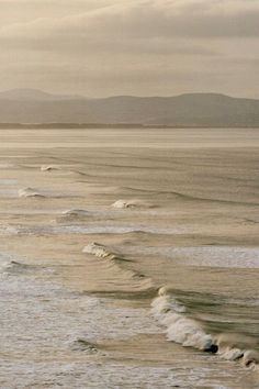 two surfers are riding the waves in the ocean on a cloudy day with mountains in the distance