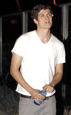 a young man is standing outside with his hands in his pockets and holding a water bottle