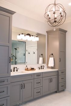 a large bathroom with two sinks and gray cabinets in the corner, along with a chandelier