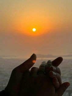 the sun is setting over the ocean as someone holds their hand out to touch it