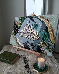 an easel sitting on top of a table with a lit candle and book next to it