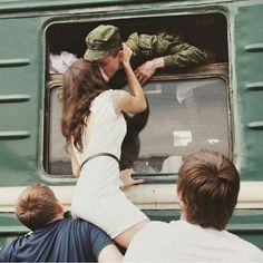 two people sitting on a train looking out the window at another person standing in front of them