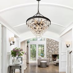 a living room filled with furniture and a chandelier hanging from the ceiling over a wooden floor