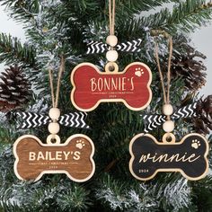 three personalized wooden dog ornaments hanging from a christmas tree with pine cones in the background