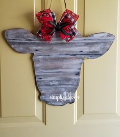 a door hanger with a cow head painted on it's side and red bows hanging from the front