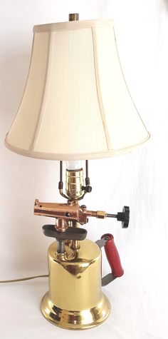 "For sale is a fascinating and unique electric lamp with industrial appeal made from shiny solid brass, cast iron, and copper welding blow torch. Circa 1910-20's. Handcrafted lamp was put together by a Math High School teacher who started his hobby in the late'70's. His goal was to create useful items out of reused and recycled materials. The welding blow torch lamp features a polished brass body with red painted wooden handle, a moving piston hand pump, cast iron holder, hard rubber valve, copp Pipe Lights, Copper Welding, Antique Lights, Car Parts Decor, Repurposed Lamp, Electric Desk, Blow Torch, Torch Lamp, Handcrafted Lamp