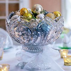 a clear glass bowl filled with ornaments on top of a white tablecloth covered table