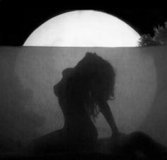 the silhouette of a woman sitting in front of a full moon with her hands behind her head