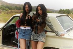 two women standing next to each other in front of a car