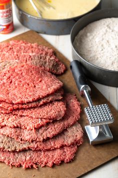 hamburger patties are stacked on a cutting board next to a skillet and other ingredients