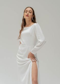 a woman wearing a white dress with a slit in the side and long sleeves on her body