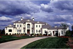 a large white house sitting on the side of a lush green field under a cloudy blue sky