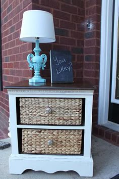 a white dresser with two wicker drawers and a blue lamp on the front porch