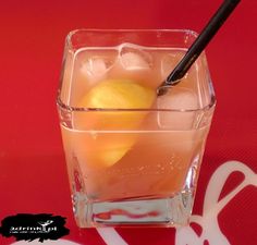 a glass filled with ice and lemons on top of a red table next to a black straw