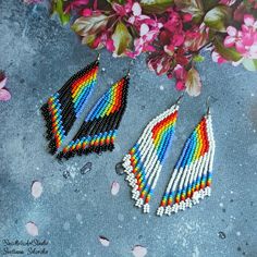 two pairs of multicolored beaded earrings next to pink flowers