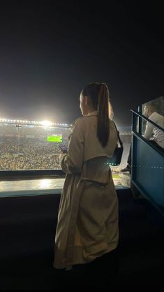 a woman standing in front of a window looking out at a football stadium filled with people