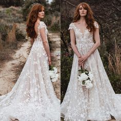 two women in wedding gowns standing next to each other on a dirt road with trees and bushes behind them