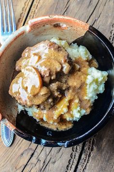 a bowl filled with mashed potatoes covered in gravy next to a fork