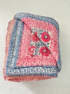 a pink and blue square pillow with flowers on it sitting on a white surface next to a wall