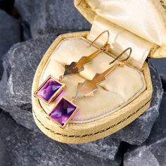 These retro drop earrings feature two rectangular cut amethysts in four prong settings. The amethysts hang from a fun geometric motif crafted in 14k rose and white gold. The earrings are finished with shepherds hook backs for pierced ears. Modern Purple 14k Gold Jewelry, Luxury Purple Rectangular Jewelry, Art Deco Gemstone Earrings For Gift, Art Deco 14k Gold Rectangular Jewelry, Purple Rectangular Jewelry For Formal Occasions, Luxury Rectangular Amethyst Jewelry, Formal Rectangular Purple Jewelry, Formal Purple Rectangular Jewelry, Modern Purple Rectangular Jewelry