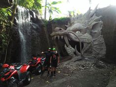 two men standing in front of a giant dragon statue with atvs parked next to it