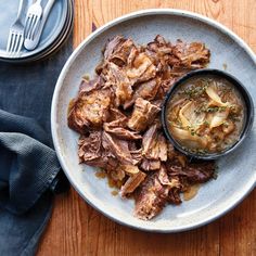 a white plate topped with meat and onions next to a bowl of soup on top of a wooden table