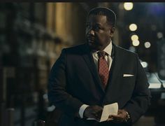 a man in a suit and tie standing on the street at night with his arms crossed