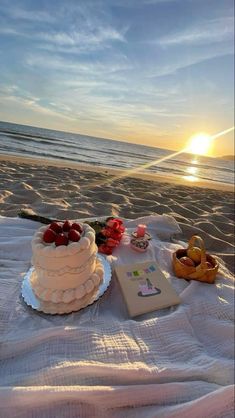 there is a cake on the beach with flowers and other things around it that are laying out in the sand