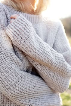 a woman with blonde hair is wearing a sweater and posing for the camera while outside