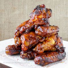 a pile of barbecue chicken wings sitting on top of a white plate covered in bbq sauce