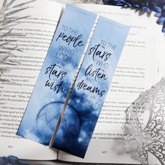 two bookmarks sitting on top of an open book with blue flowers in the background