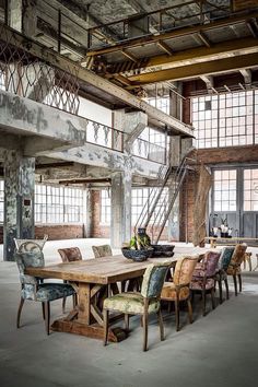 a large wooden table surrounded by chairs in an industrial setting with exposed ceilings and windows