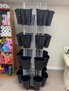 several black plastic pots are stacked on a metal rack in front of a shelf with scissors and other craft supplies