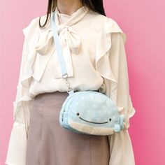 a woman wearing a white blouse and gray skirt holding a blue whale purse with her face close to the camera