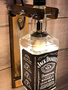 an old fashioned jack daniels whiskey bottle hanging on a wooden wall with a hook in it