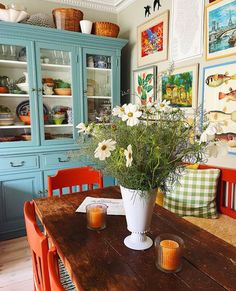 a vase with flowers sitting on top of a wooden table in front of blue cabinets