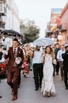 a bride and groom walking down the street with umbrellas